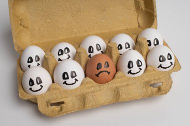 Kağıt tepsi dolusu gülümseme beyaz yumurtalar ve sadece bir farklı üzgün portakal yumurtası. Ayrımcılık, yabancı düşmanı, ırkçı kavram.