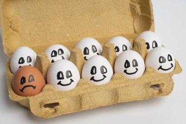 Kağıt tepsi dolusu gülümseme beyaz yumurtalar ve sadece bir farklı üzgün portakal yumurtası. Ayrımcılık, yabancı düşmanı, ırkçı kavram.