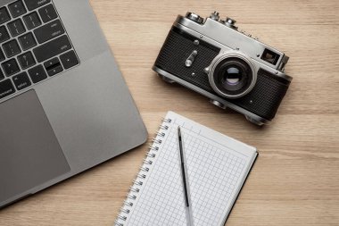 Üst görünüm ofis fotoğraf masası, dizüstü bilgisayarı, defteri, kamerası ve kalemi var..