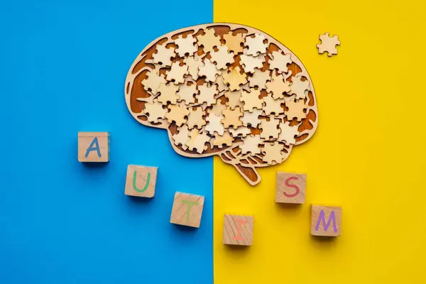 stock image Mock up of a human brain with scattered puzzle pieces on a yellow and blue background. Six cubes with the inscription autism.