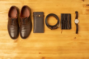 Kahverengi deri cüzdanlı erkek aksesuarları, kemer, defter, ayakkabı ve ahşap arka planda saat.