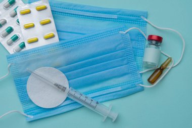 Şırınga, maske, tabletler, mavi arka planda ampuller, aşı kavramı.
