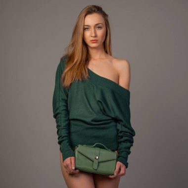 Stüdyoda zümrüt kazakla poz veren güzel bir genç kadın.