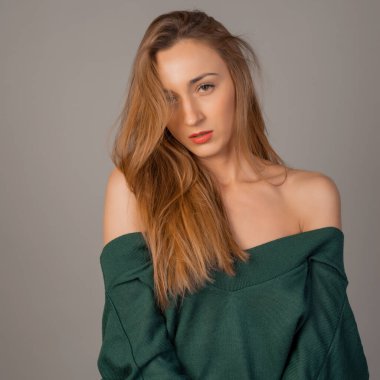 Stüdyoda zümrüt kazakla poz veren güzel genç bir kadın.