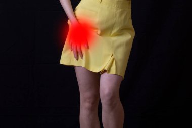 Siyah arka planda kalça eklemi ağrısı çeken genç bir kadın..