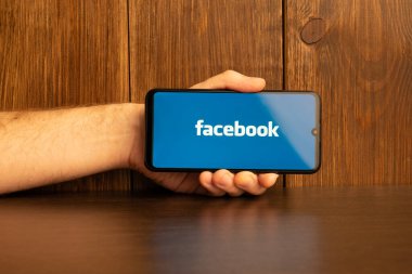 Kyoto Şehri, Japonya - 31 Temmuz 2023: Akıllı telefon ekranındaki Facebook logosu ahşap masa arkasındaki Apple Macbook klavyesine yerleştirildi.