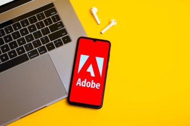 Kyoto Şehri, Japonya - 31 Temmuz 2023: Akıllı telefon ekranındaki Adobe logosu sarı masa arkasındaki Apple macbook klavyesine yerleştirildi.