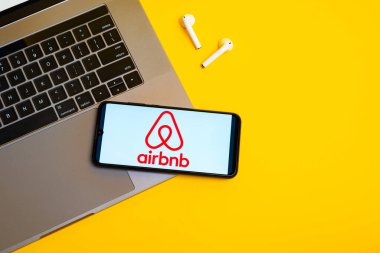 Kyoto Şehri, Japonya - 31 Temmuz 2023: Sarı arka planda modern bir dizüstü bilgisayarın yanında akıllı bir telefonla logo Airbnb
