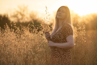 Leopar desenli elbiseli güzel bir kadın gün batımında bir tarlada poz veriyor.