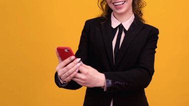 Mutlu genç bir kadının fotoğrafı. Sarı duvar arkasında cep telefonuyla izole edilmiş poz veriyor..