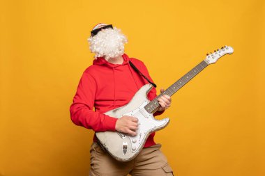 Modern Noel Baba rock n roll çalar gitar çalar duygusal olarak sarı arka planda izole olur