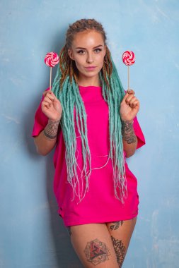 Dövmeli, rastalı, üzerinde şeker lolipopları olan pembe bir tişörtle poz veren güzel bir kız.