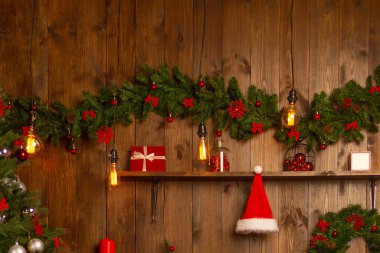 Ahşap bir duvarın arkasında çelenk olan Noel ağacı.