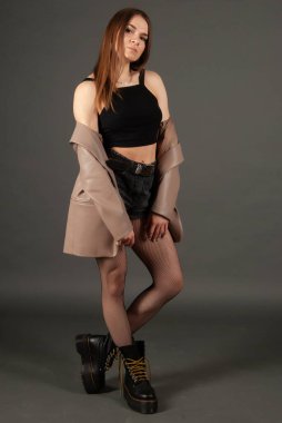 Siyah kot şort ve kahverengi deri ceketli çizme giyen güzel bir kızın portresi. Stüdyo arka planında tam boy ayakta poz