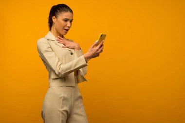 Sarı arka planda akıllı telefonla poz veren cilt sorunu olan genç bir kız..