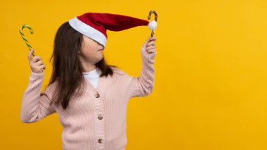 Noel Baba 'nın Noel şapkalı genç kız ellerinde şekerlemelerle sarı bir arka planda