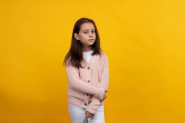 Pembe ceketli ve beyaz pantolonlu genç bir kız sarı arka planda poz veriyor.