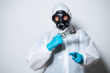 COVID-19 (Coronavirus) 'a karşı gaz maskeli koruma kıyafeti giyen bir doktor beyaz arka planda şırınga ve aşı bulundurur.