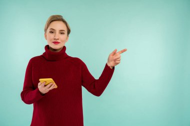 Kırmızı kazaklı, mavi arka planda akıllı telefonu olan neşeli bir kız.