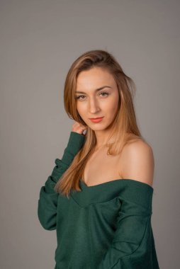 Stüdyoda zümrüt kazakla poz veren güzel genç bir kadın.