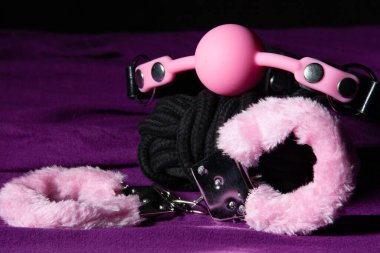 Bdsm kıyafeti. Kölelik kelepçesi ve mor çarşafın üzerinde ağız tıkacı topu. Yetişkin seks oyunları. Sapıkça yaşam tarzı.