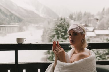 Kadın balkonda battaniyeye sarılmış.