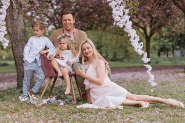 Spring. Happy family siting in sakura park. Mother, father and s