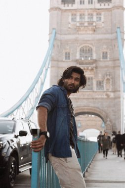 Londra 'daki yakışıklı Hintli stil sahibi adam Londra Köprüsü' nün karşısında. O bir kot ceket giyiyor ve kameradan uzağa bakıyor. Yüksek kalite fotoğraf