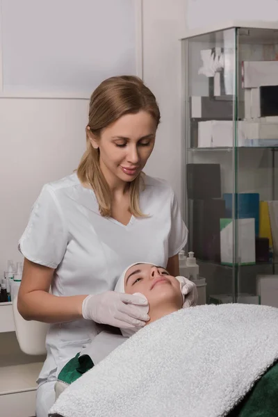 stock image Top view of crop unrecognizable cosmetician using cotton pads and applying tonic on face of female customer lying on table in beauty salon during skincare procedure. High quality photo