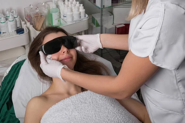 stock image Beautician gives protective eyeglasses for female patient on before laser hair removal procedure. High quality photo