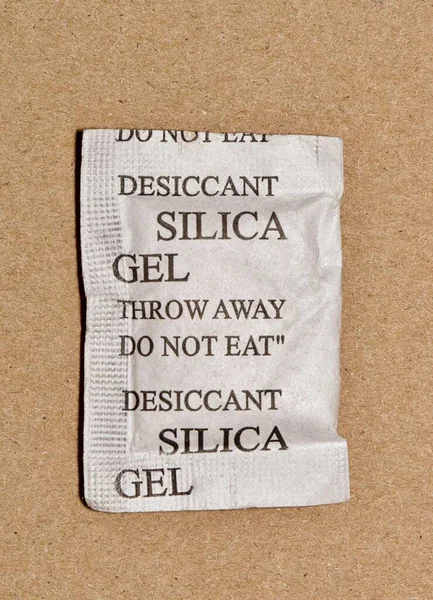 Single Silica gel packet isolated in a cardboard box, flat lay format. Porous desiccant substance used in packing material to absorb humidity moisture.