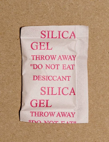 Single Silica gel packet isolated in a cardboard box, flat lay. Porous desiccant substance used in packing material to absorb humidity moisture.