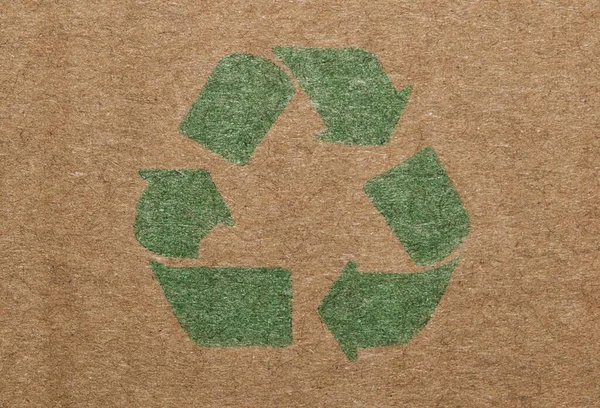 Green recycle symbol printed on a cardboard box, closeup isolated macro view.