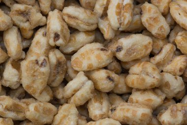Dry honey puffed wheat cereal pieces scattered loosely directly above. Breakfast foods textured background, full frame image.
