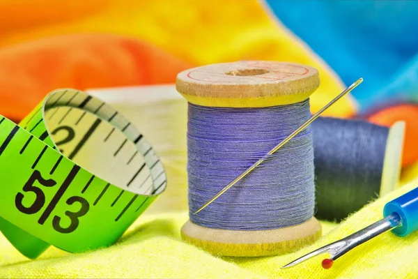 Sewing item tools on colored clothing with macro details including spools of thread, needle, tape measure and thread picker.