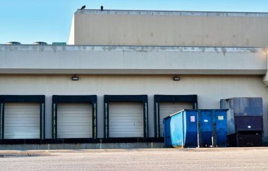 Mavi çöp konteynırları olan endüstriyel bir deponun arkasındaki kapalı rıhtım kapıları. Çöp öğütme ve geri dönüşüm alanı.