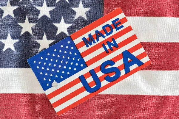 Made in USA product label sitting on top of a partial American flag as an economy concept. Macro image with patriotic background details.