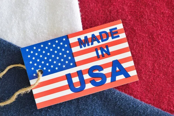 Made in USA label sitting on top of red, white and blue clothing shirts as a business economics concept. Flat lay macro image with patriotic background details.