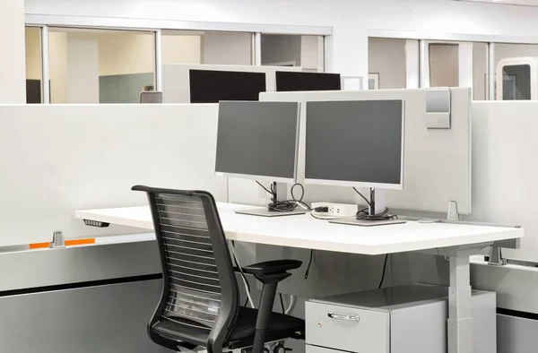 Empty office desk space with computer monitors, desk and chair at a cubicle. Working from home concept image.