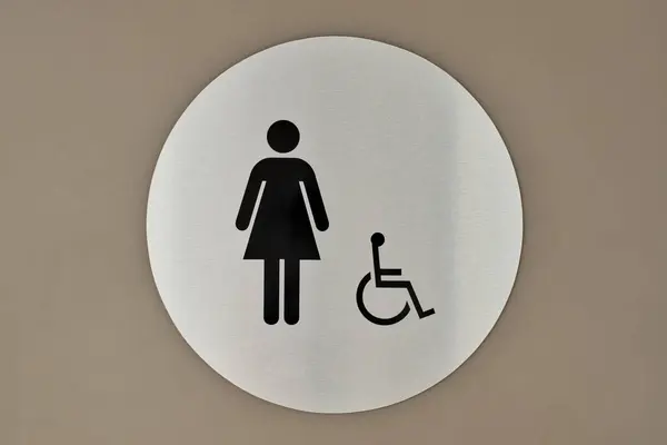 Women\'s bathroom and handicap sign on a wall. Circular sign and symbol designation placard.