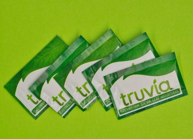 Houston, Teksas ABD 05-14-2025: Beş Truvia yapay tatlandırıcı paketleri stevia yaprağı yeşil arkaplan fotokopi alanına saçıldı.