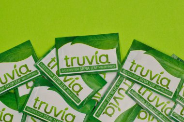Houston, Teksas ABD 05-14-2025: Truvia yapay tatlandırıcı paketleri stevia yaprağı yeşil zemine saçıldı.