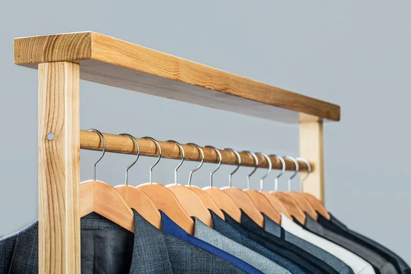 Mens shirts, suit hanging on rack. Hangers with jackets on them in boutique. Suits for men hanging on the rack. Mens suits in different colors hanging on hanger in a retail clothes store, close-up.