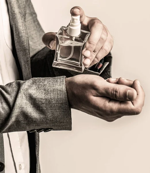 Fashion cologne bottle. Man holding up bottle of perfume. Men perfume in the hand on suit background. Man in formal suit, bottle of perfume, closeup.