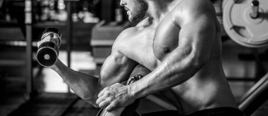 Spor salonunda dambılı kaldıran bir adam kas egzersizi yapıyor. Vücut geliştirici, dambıllarla egzersiz yapıyor. Fitness adamı dambılı kaldırıyor. Siyah ve beyaz.