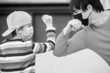 Koruyucu önlemler. Babası oğluna dışarıda bir yüz koruyucu maske takıyor. Siyah ve beyaz.