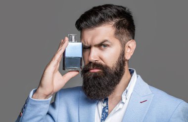 Sakallı adam parfüm şişesi tutuyor. Moda kolonya şişesi. Sakallı erkek pahalı koku kokusu tercih eder. İnsan parfümü, koku. Erkeksi parfüm. Erkek koku ve parfümeri, kozmetik.