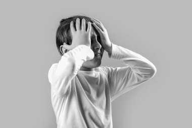 Little boy having a headache. Despair, tragedy. Portrait of a sad boy holding his head with his hand, isolated on the gray background. Black and white.