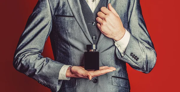 Man in formal suit, bottle of perfume, closeup. Men perfume in the hand on suit background. Fragrance smell.