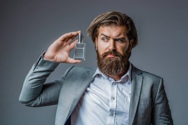 Male holding up bottle of perfume. Perfume or cologne bottle and perfumery, cosmetics, scent cologne bottle, male holding cologne. Masculine perfume, bearded man in a suit.